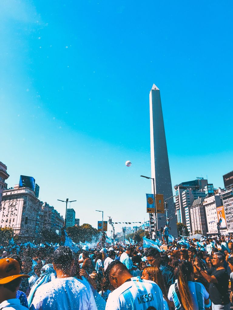 A vibrant crowd gathers at Buenos Aires' iconic Obelisk, celebrating a joyous occasion under the clear blue sky.