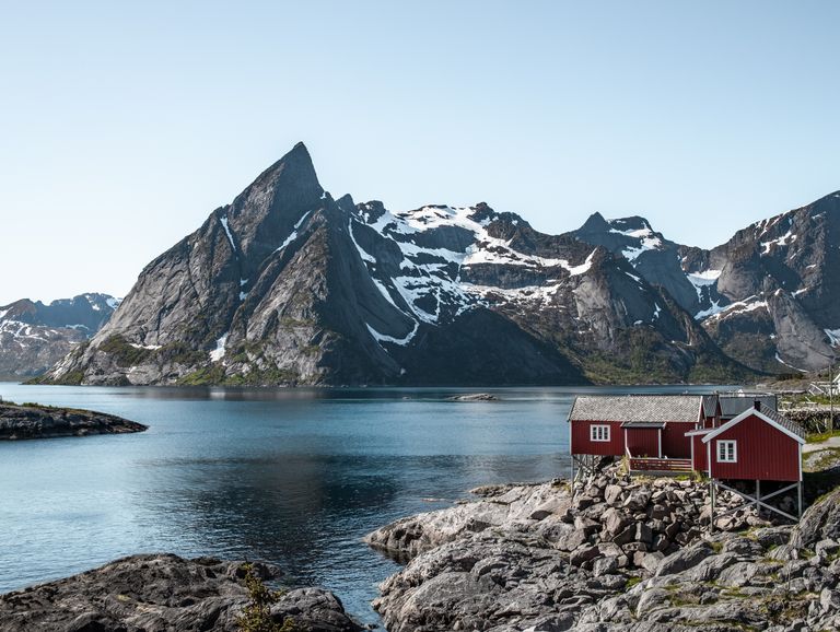 A picturesque coastal village with red cabins against the scenic backdrop of Nordland's majestic mountains.