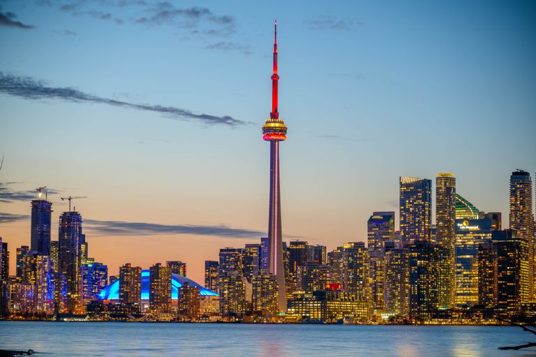 Beautiful sunset view of Toronto skyline with CN Tower and city lights reflecting on the lake.