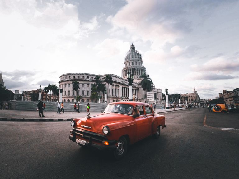 Classic red car in vibrant Havana street, with Capitol Building in the background, creating a timeless urban scene.