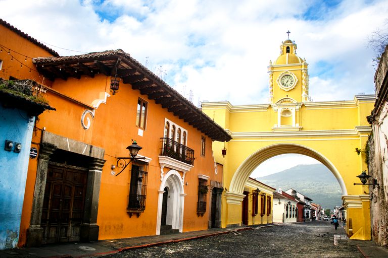 Colorful street with Santa Catalina Arch in Antigua, Guatemala. Vibrant colonial architecture and scenic mountainous backdrop.