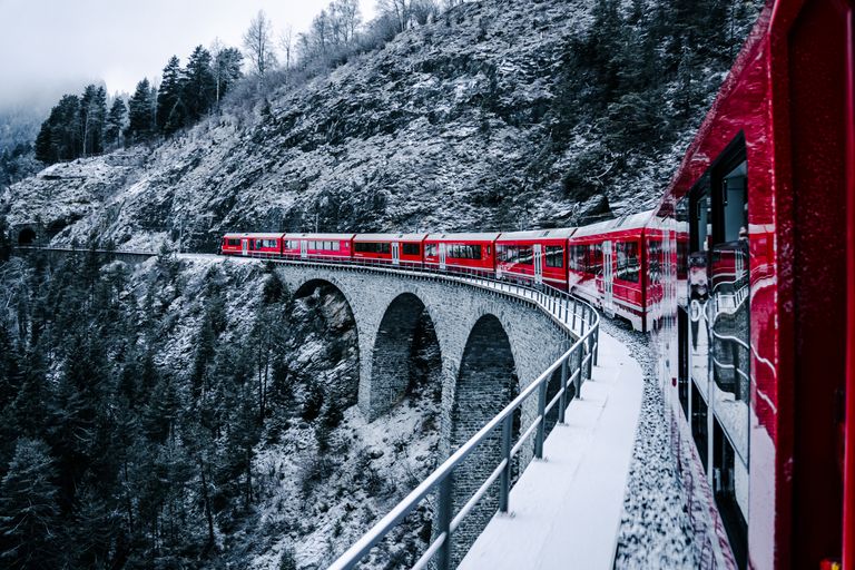 Scenic view of a red train on a snow-covered bridge in the Swiss Alps, showcasing winter beauty.