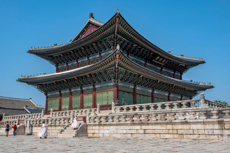 Traditional architecture of Gyeongbokgung Palace, Seoul, with visitors in traditional hanbok attire.