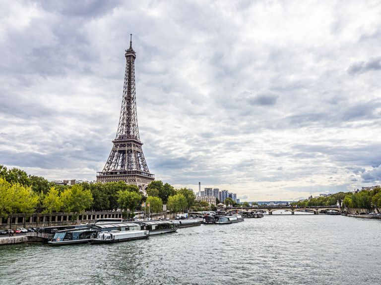 Scenic view of the Eiffel Tower by the Seine River under a cloudy sky in Paris, France.