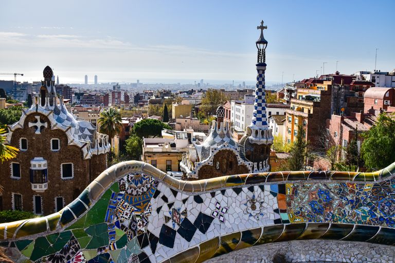 Gaudí's iconic mosaic architecture in Park Güell with a view of Barcelona's cityscape.
